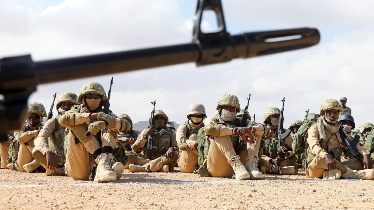 soldiers are sitting in the sand with their weapons in hand